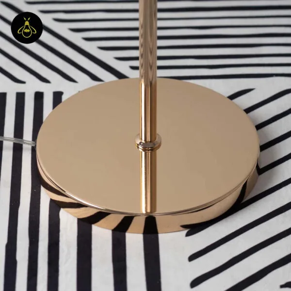 Close-up of the polished gold round base and slim stem of the amber glass sphere floor lamp