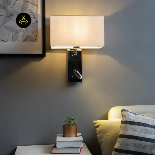 Wall mounted bedside light lit above a nightstand with books in a grey bedroom