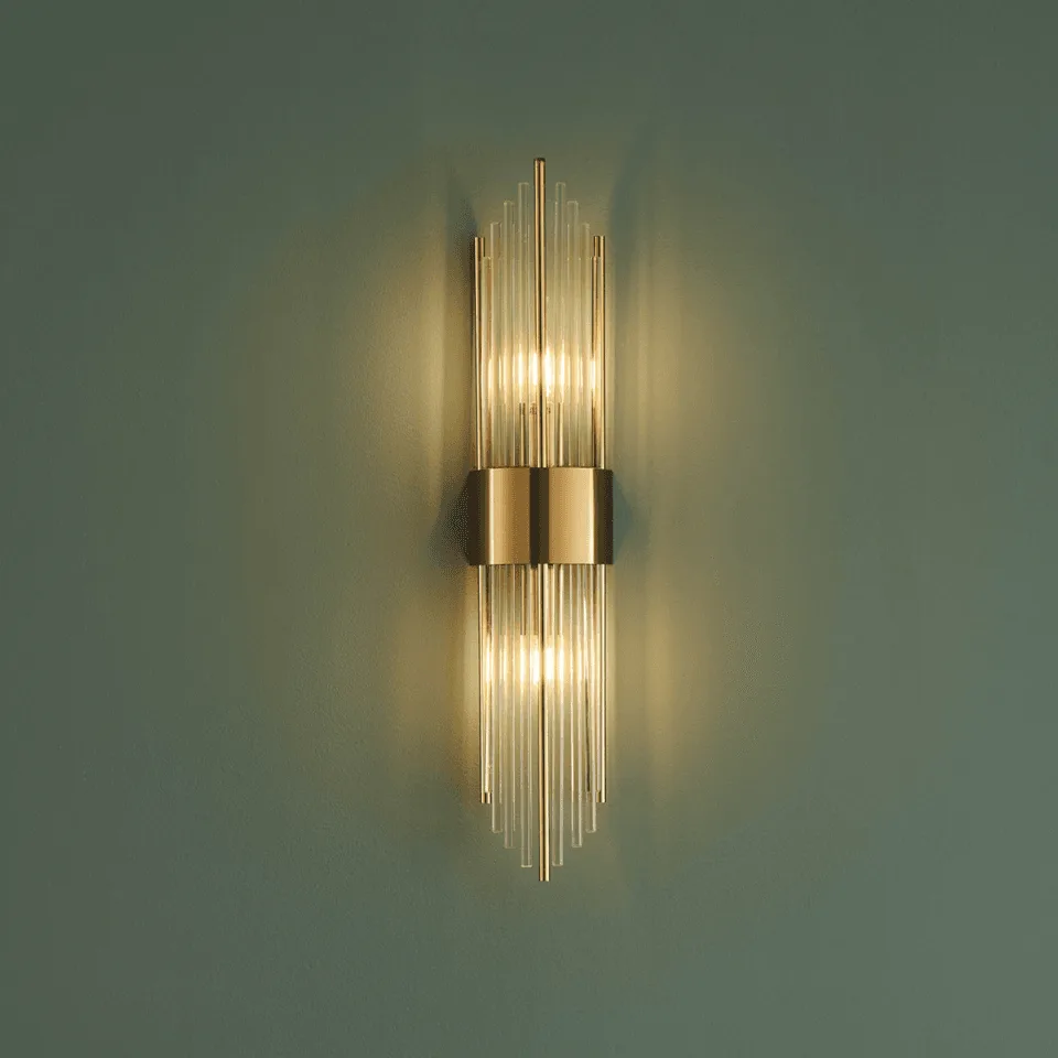 Art deco wall light, Dania, lit on a green wall: clear borosilicate glass rods around a gold-finish stainless steel band