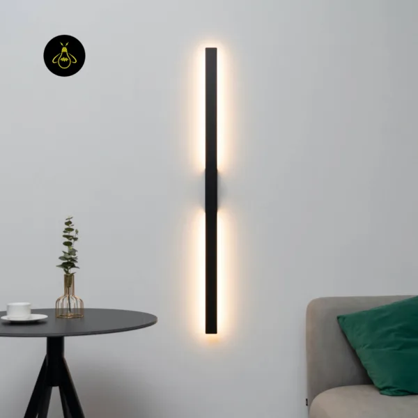 Slim LED wall light mounted vertically in a living room beside a grey sofa and round side table, glowing warm along both halves