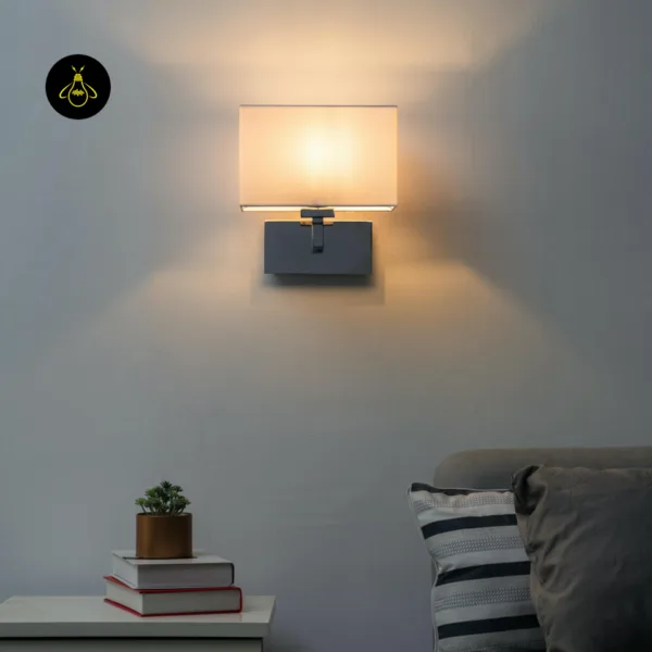 Wall lamp with shade lit above a bedside table and sofa, washing warm light up and down a grey wall