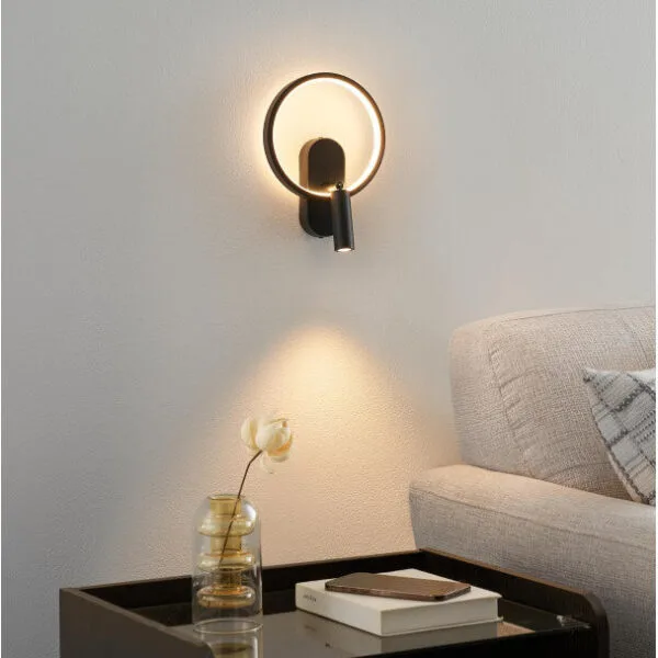 Black circle wall light with its reading spot lit beside a sofa in a living room