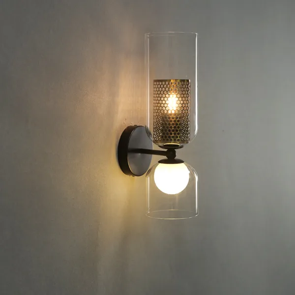 Double wall light with a clear borosilicate glass cylinder, honeycomb cage and opal globe, lit on a grey wall