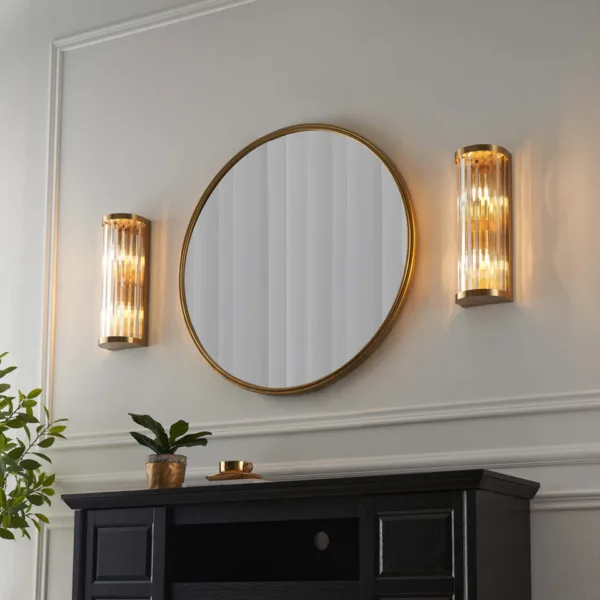 Pair of ribbed glass wall lights glowing either side of a round mirror above a black console in an entryway