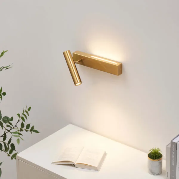 Satin gold wall reading lamp lighting an open book on a white desk