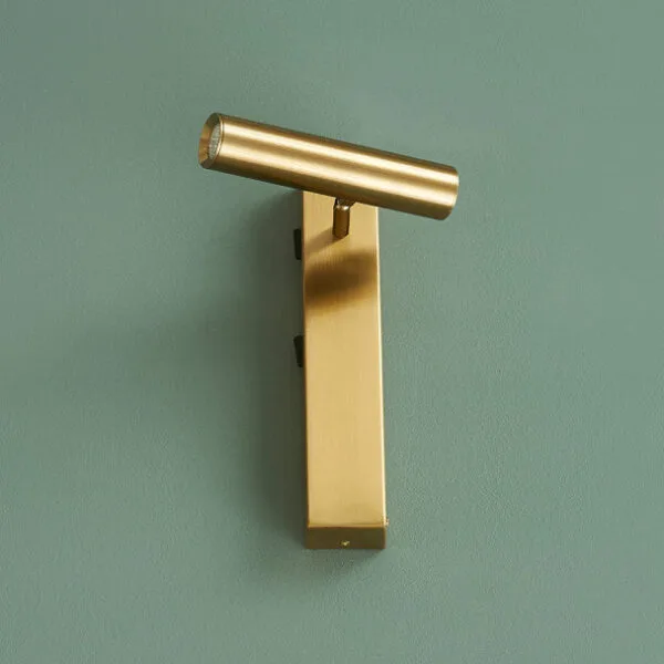 Satin gold wall reading lamp mounted upright on a green wall, reading head turned across the top
