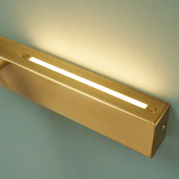 Close-up of the brushed satin gold backplate with the LED up-light slot glowing on the wall reading lamp