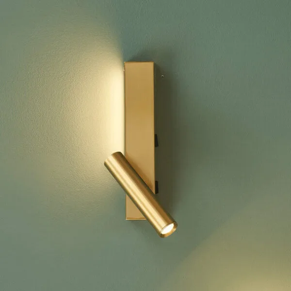 Satin gold wall reading lamp mounted upright on a green wall, reading head angled down and lit
