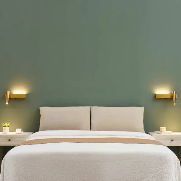 A pair of satin gold wall reading lamps either side of a bed against a sage green wall