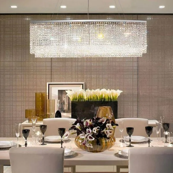 Oval crystal chandelier lit over a white dining table, two tiers of K9 crystal in a chrome frame