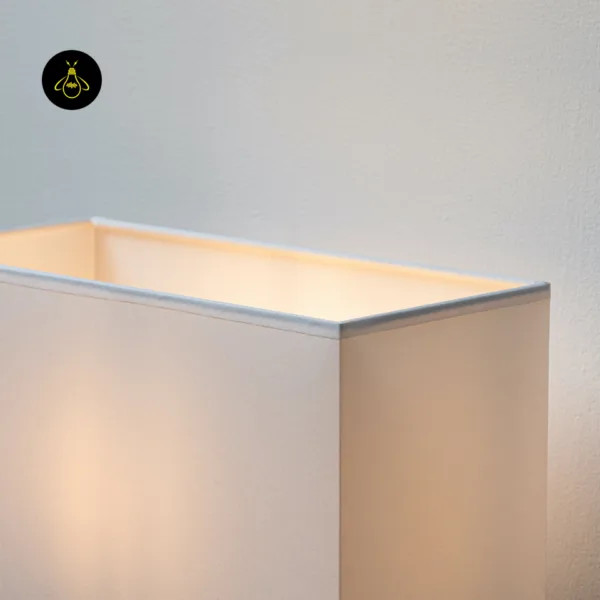 Close-up of the bound top edge of the white fabric shade on the wall lamp with shade, glowing warm inside