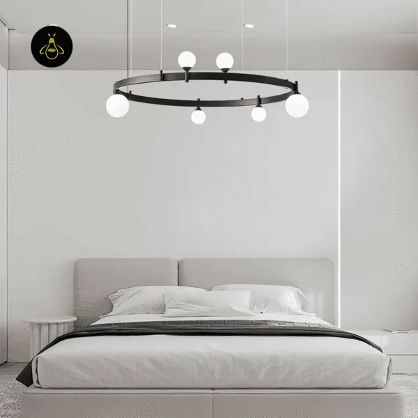 Black circle chandelier glowing with six opal globes above a grey upholstered bed
