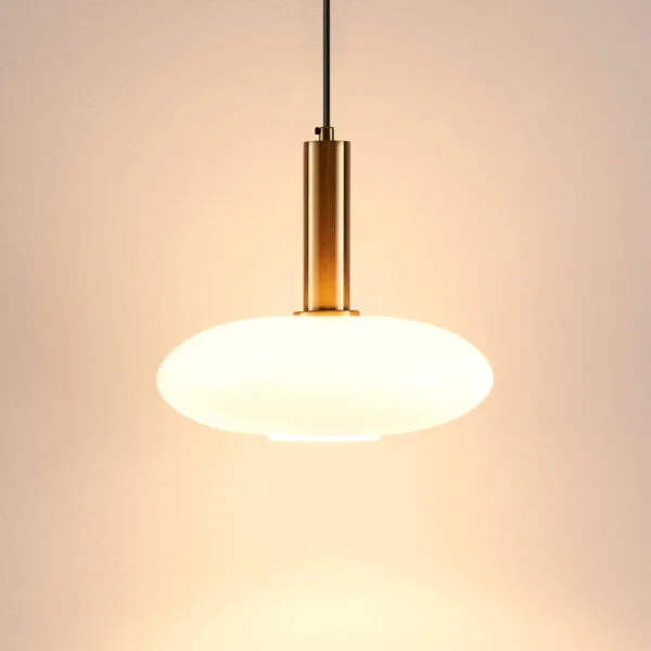 Opaline glass pendant light glowing warm against a peach wall, brushed gold holder above the opal shade