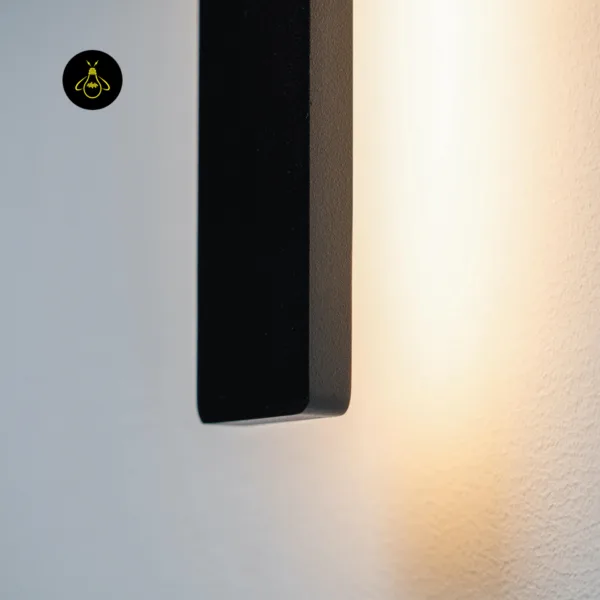 Close-up of the slim LED wall light end in matte black stainless steel with warm light washing the textured wall