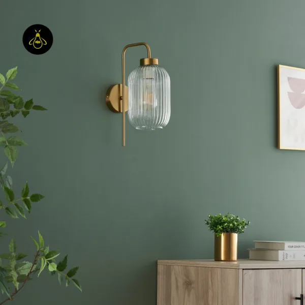 Fluted glass wall light switched off on a sage green wall, clear ribbed glass shade and gold arm