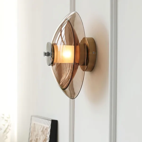 Amber glass wall light lit on a white panelled wall, side view of the saucer and chrome stainless steel centre cap