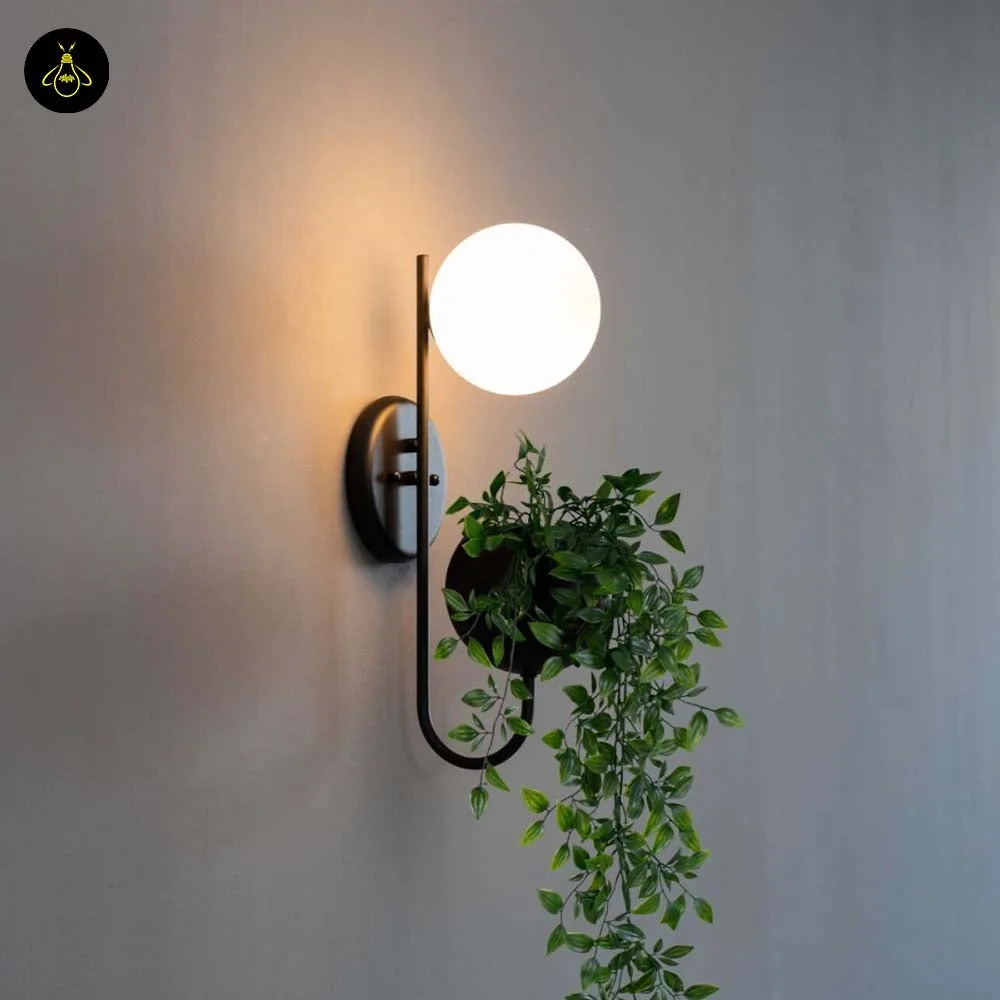 Plant pot wall light in matte black with lit opal globe and trailing plant