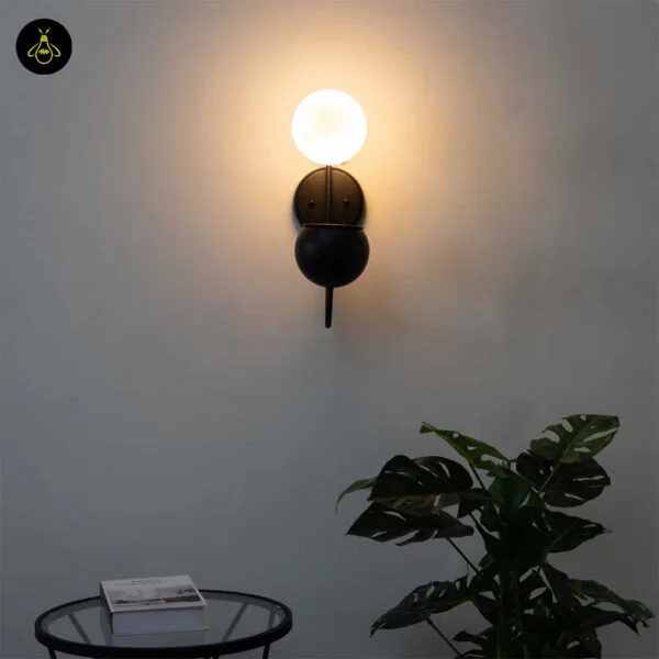 Front view of the lit plant pot wall light above a glass side table and a monstera plant