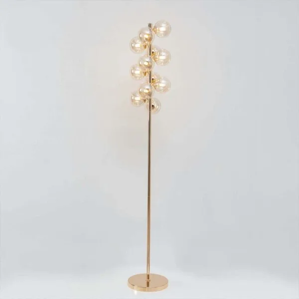 Full-length gold floor lamp with amber glass spheres lit, on a white background