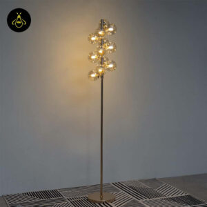 Gold floor lamp with amber glass spheres creating a warm glow on a plain background