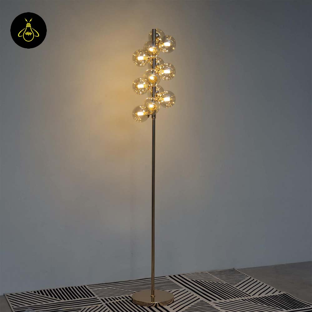 Gold floor lamp with amber glass spheres creating a warm glow on a plain background