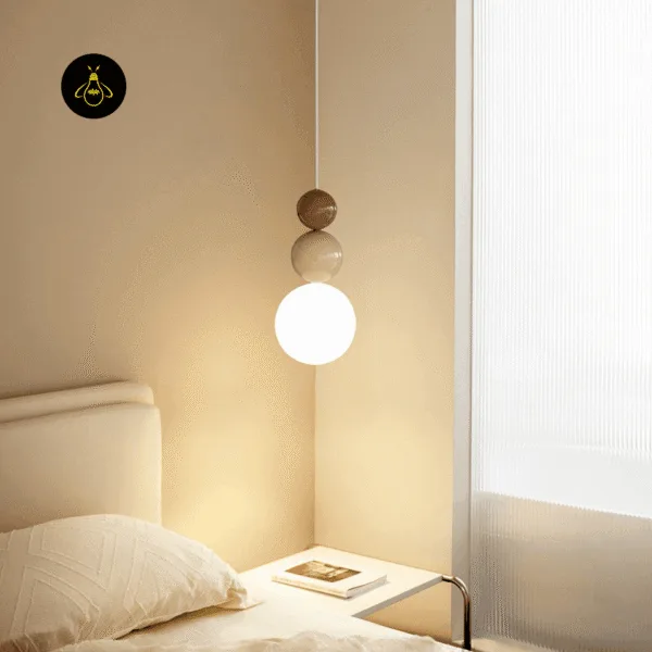 Glass ball pendant light lit beside a bed and a window in a warm cream bedroom