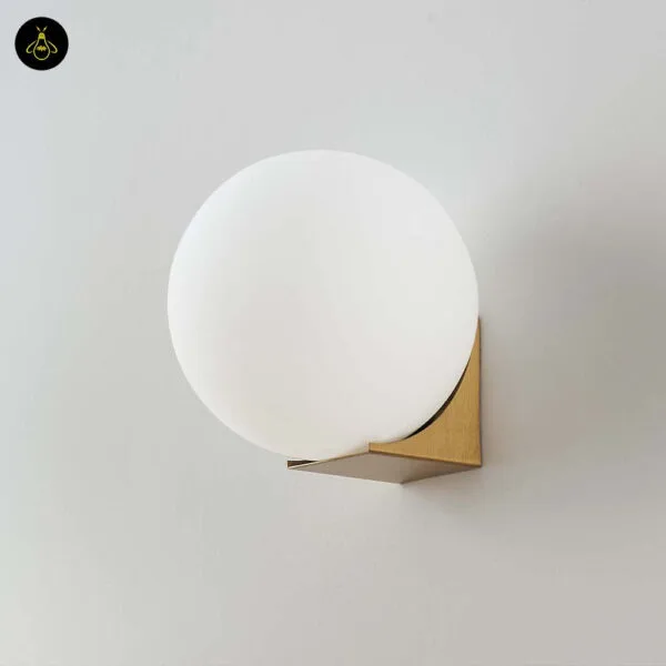 Globe wall light switched off, opal borosilicate glass ball on a brushed-gold base, front view