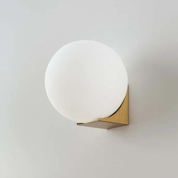 Globe wall light switched off, opal borosilicate glass ball on a brushed-gold base, front view