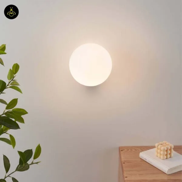 Globe wall light lit on a cream wall in a living room beside a plant and a wooden side table