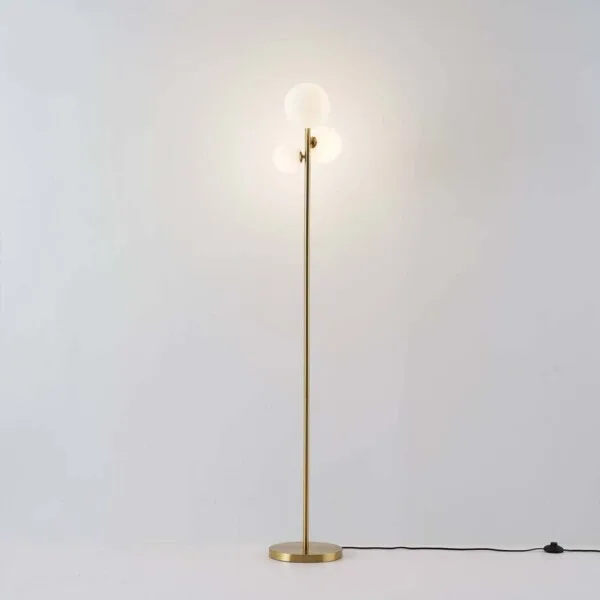 Full-length glass globe floor lamp, 150 cm brushed gold stem with three lit opal globes, on a plain light background