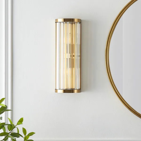 Ribbed glass wall light switched off on a panelled wall next to a round gold mirror