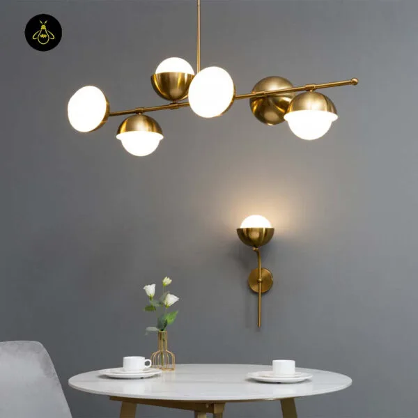 Opal white light glowing on a grey wall below a brass multi-globe chandelier, above a round marble table set with cups