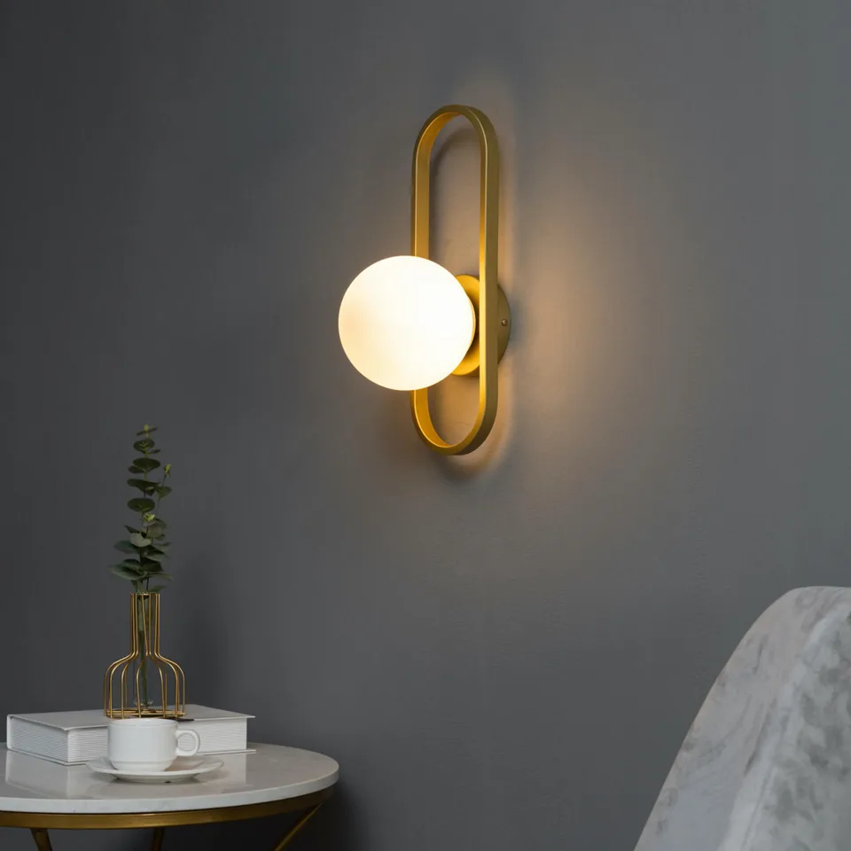 Vintage wall sconce in gold with a white opal glass globe on an oblong frame for a bedroom wall