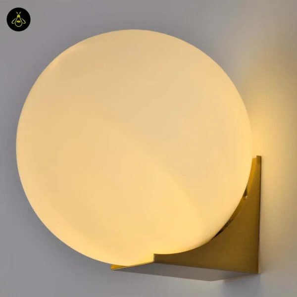 Globe wall light lit, warm opal borosilicate glass ball on a brushed-gold base, close view