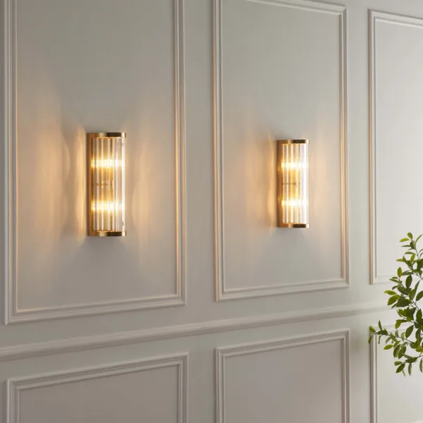 Two ribbed glass wall lights glowing on a white panelled hallway wall