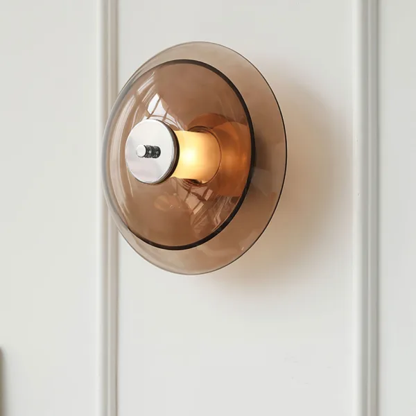 Amber glass wall light on a panelled wall, three-quarter front view of the round amber borosilicate glass saucer and chrome cap