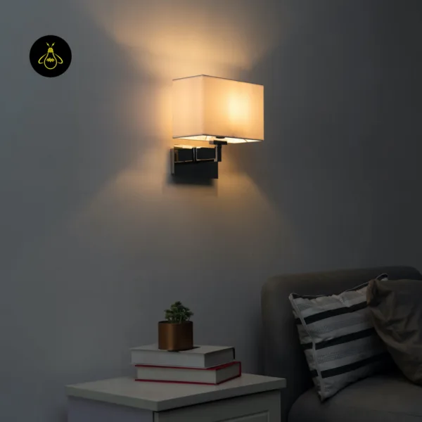 Wall lamp with shade lit on a dark grey wall above a bedside table with books