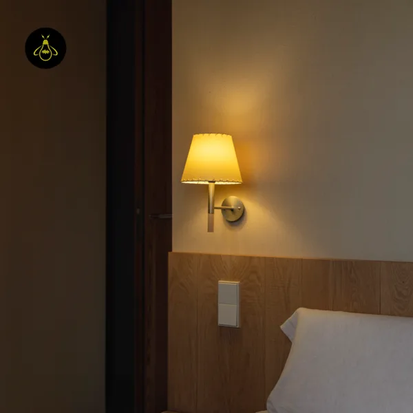 Lit fabric wall light with a stitched-edge shade above a wood-panelled bedhead