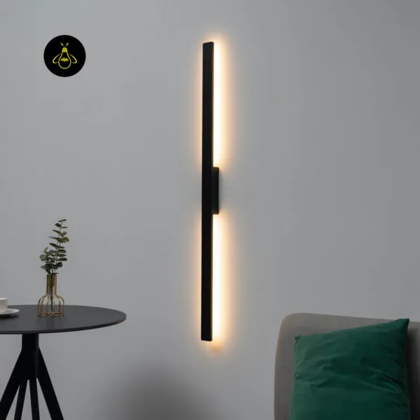 Slim LED wall light glowing vertically on a living room wall above a sofa with a green cushion and a black side table
