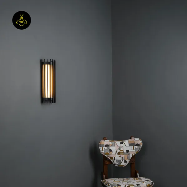 Modern outdoor wall light mounted on a grey wall, glowing warm through black slats, with a patterned chair below