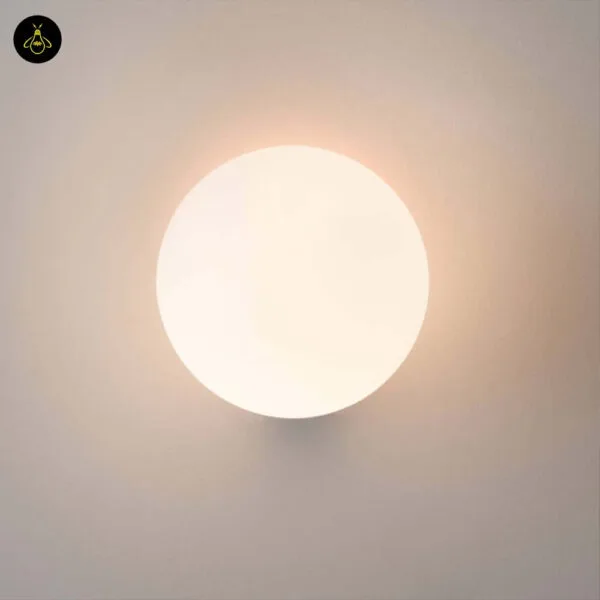 Globe wall light lit, the opal borosilicate glass ball glowing warm white with the base hidden behind it