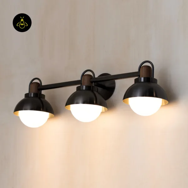 Vanity wall light at an angle showing walnut wood collars, gloss black domes with brass-finish lip ring and round backplate