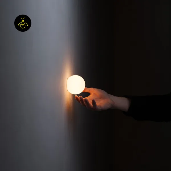 Hand beneath the lit 6.7 cm globe of the alabaster wall light, showing its compact size