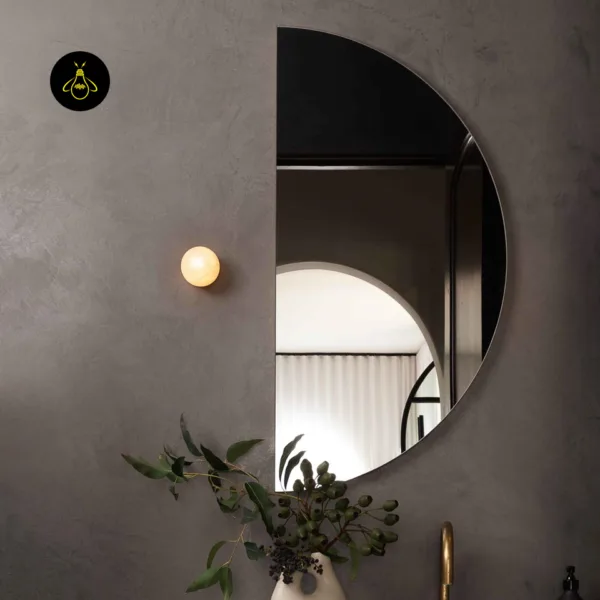 Alabaster wall light beside a half-round mirror above a bathroom vanity with a brass tap
