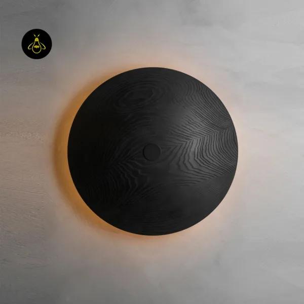 Wooden wall light from the front: round 51 cm black wood disc with a warm halo glowing on a grey plaster wall