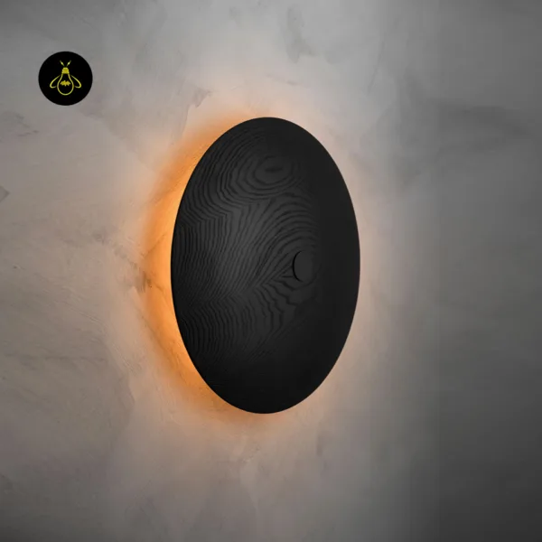 Wooden wall light switched on at an angle, warm halo spreading onto the wall from behind the black wood disc