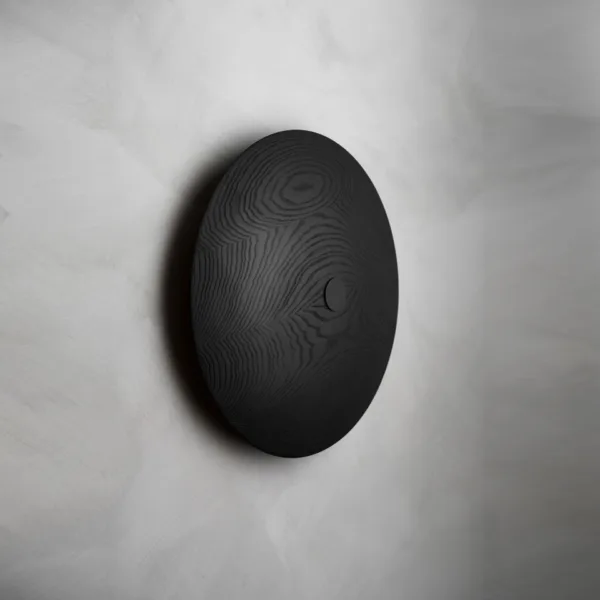 Wooden wall light from the side, switched off: matte black solid-wood disc with visible grain and a small centre cap