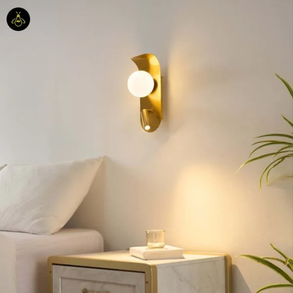 Bedroom reading light in brushed gold with a lit opal borosilicate glass globe and reading spot, fixed on a white wall above a marble bedside table