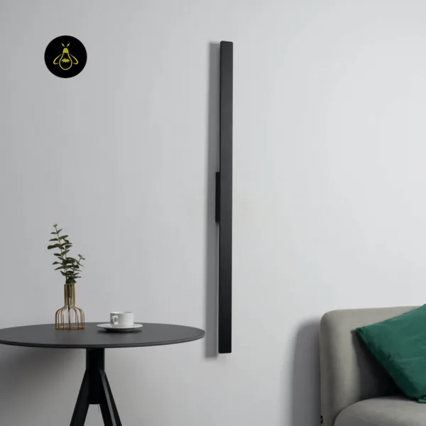 Slim LED wall light switched off, a flat matte black stainless steel bar standing upright beside a sofa and side table