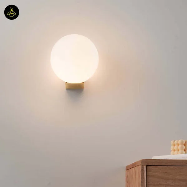 Globe wall light lit on a cream living room wall above a wooden sideboard